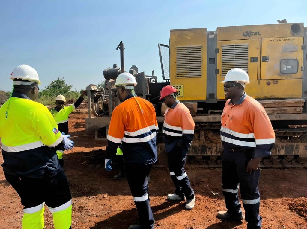 Équipe de techniciens en tenue de sécurité discutant devant une foreuse sur un site minier, sous un ciel dégagé